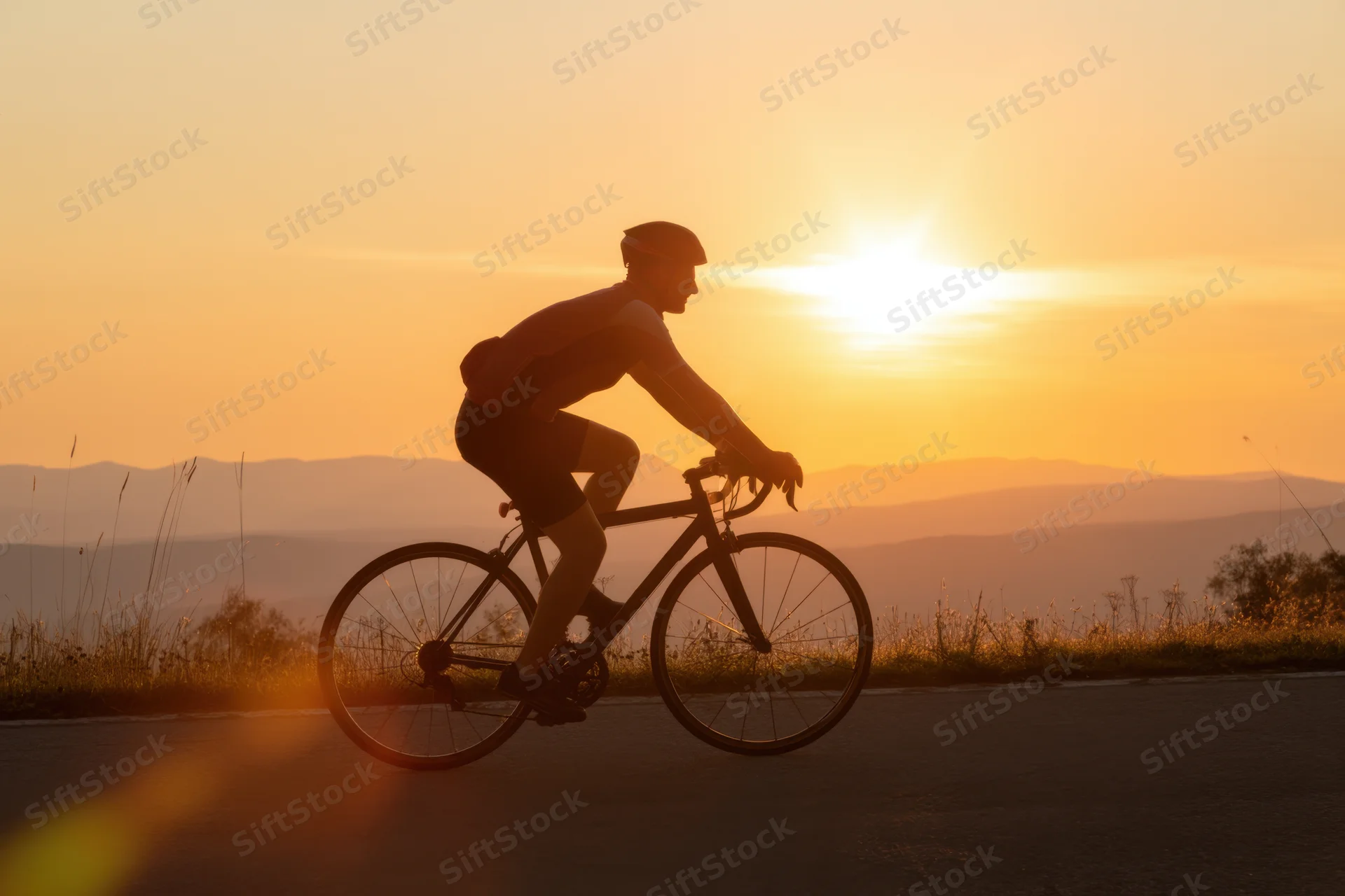 Silhouette of a cyclist riding a bicycle on a road at sunset with mountains in the background