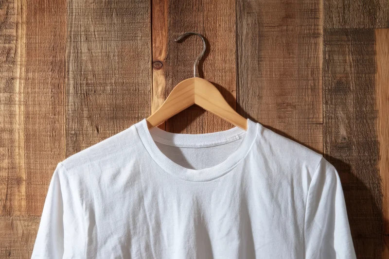 White t-shirt hanging on wooden hanger against wood panel wall