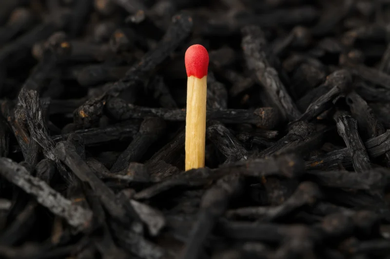 Single matchstick with red head standing upright among burnt match remnants
