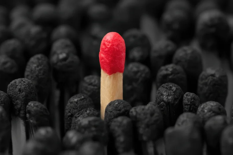 Single red matchstick standing upright among black matchsticks in close-up view