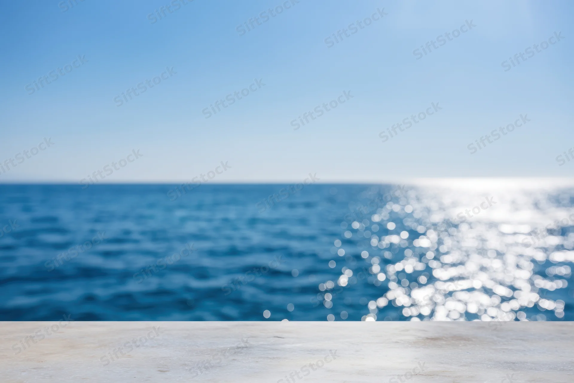 Smooth marble tabletop in foreground with blurred ocean and sky background