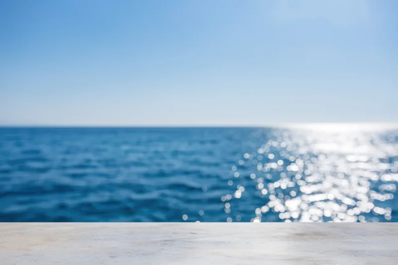 Smooth marble tabletop in foreground with blurred ocean and sky background