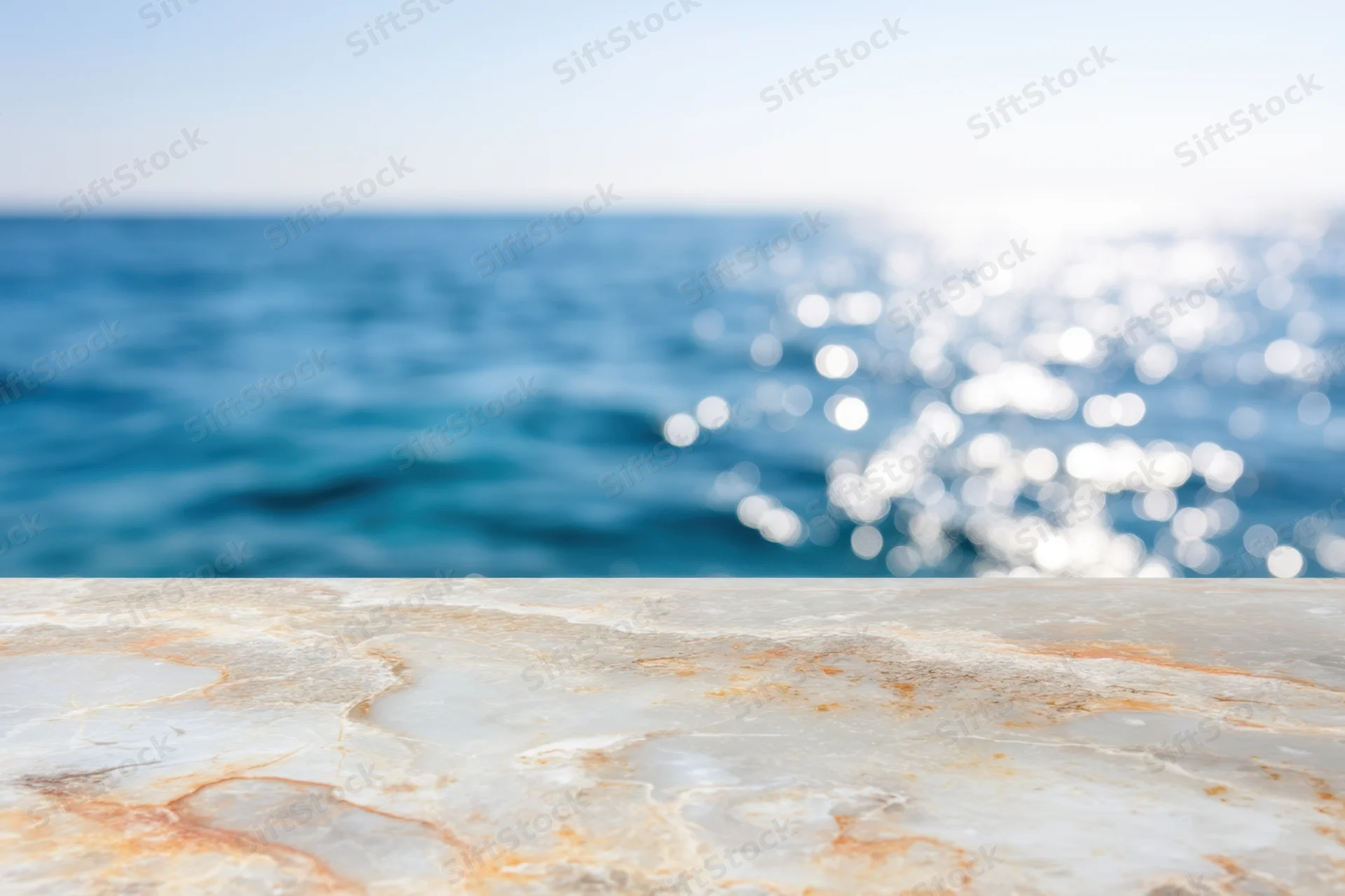 Smooth marble tabletop in foreground with blurred ocean and sunlight in background