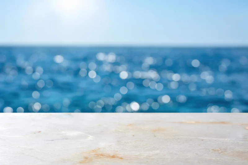 Smooth marble tabletop in foreground with blurred ocean and sky in background