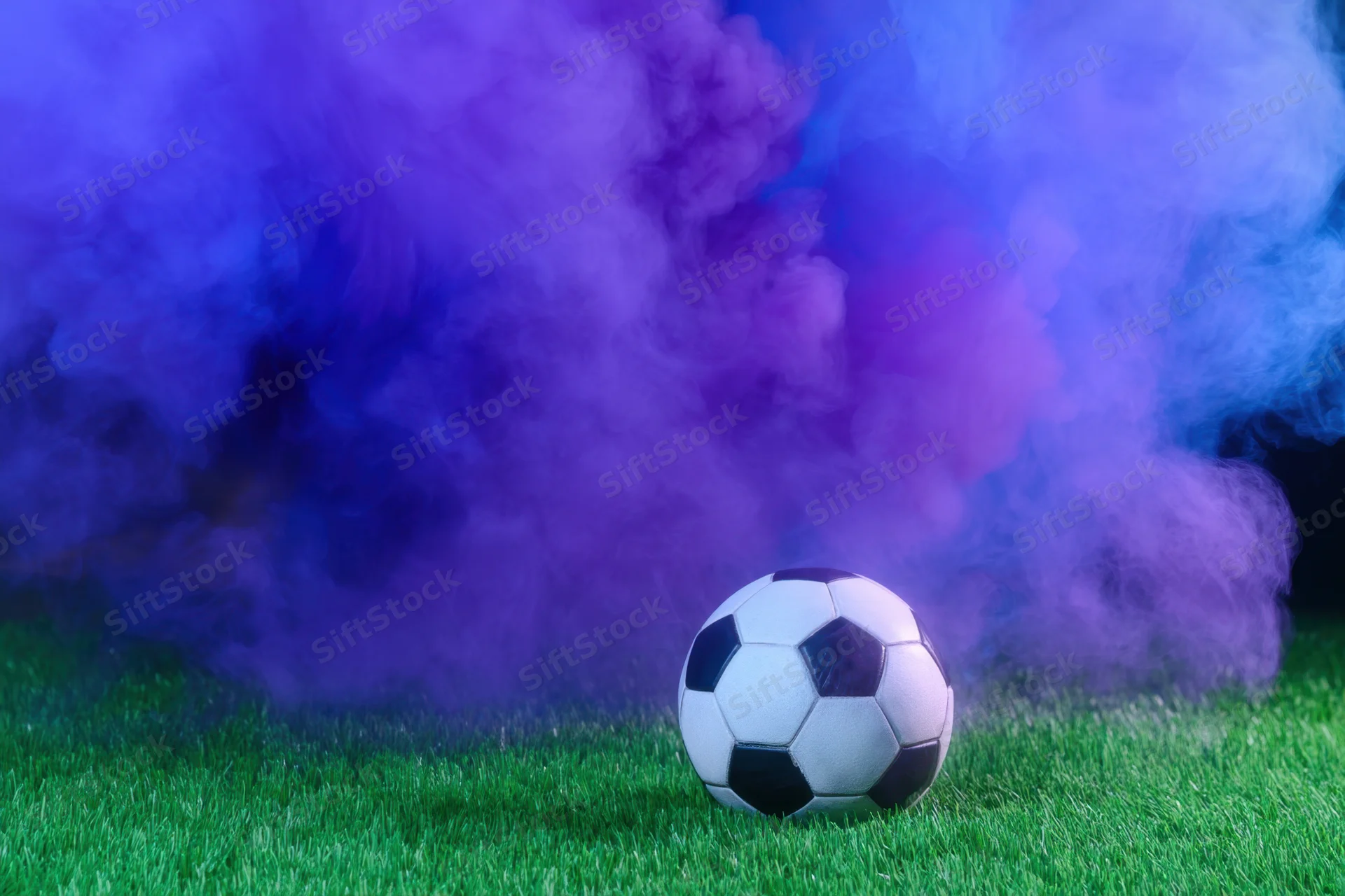 Soccer ball resting on green pitch surrounded by purple and blue smoke