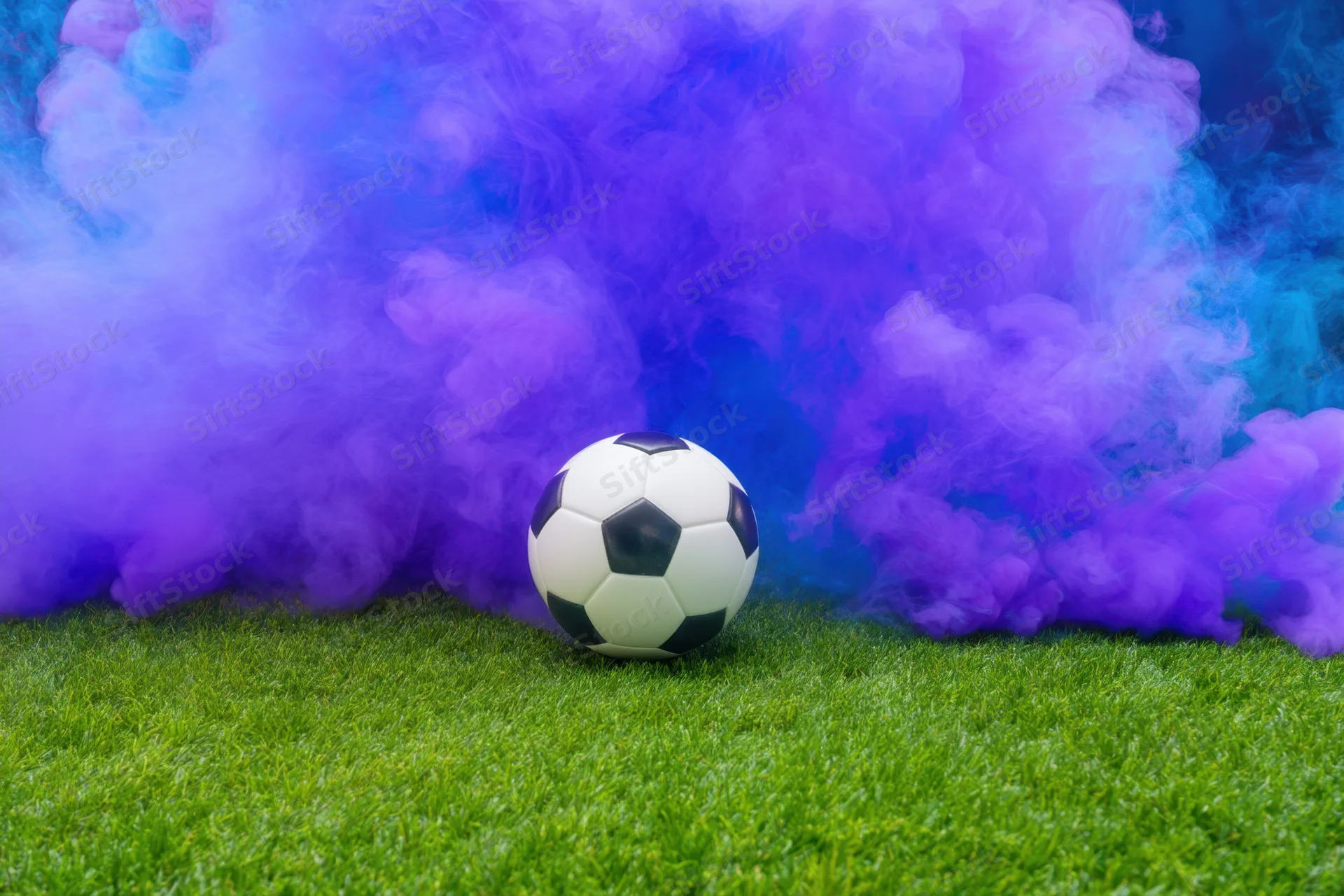 Soccer ball resting on green pitch surrounded by purple and blue smoke