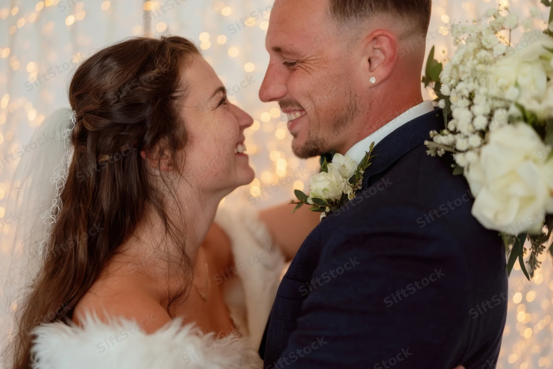Bride and groom smiling at each other in front of warm glowing bokeh lights