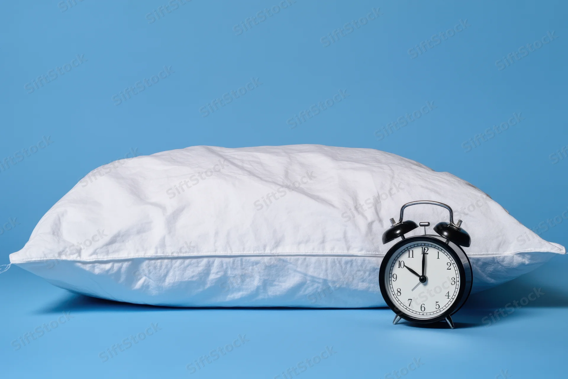 White plush pillow with black alarm clock on blue background