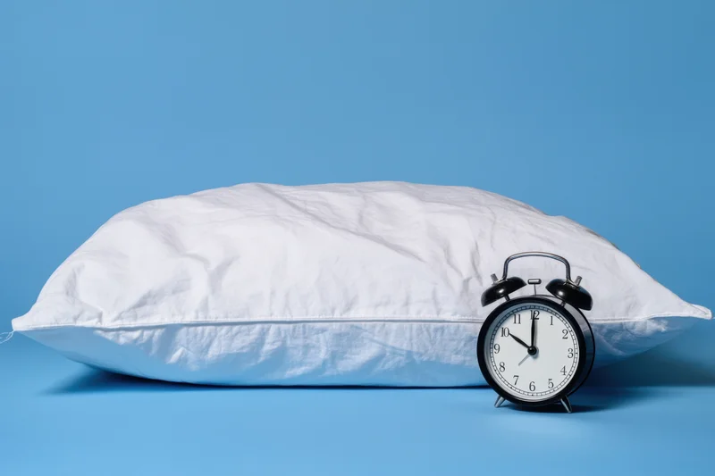 White plush pillow with black alarm clock on blue background