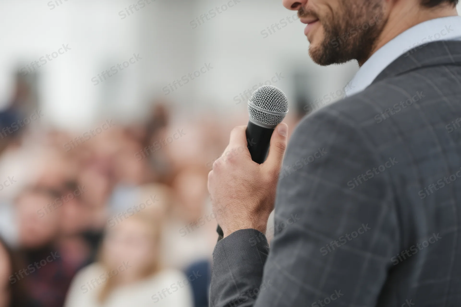 Man in suit holding microphone speaking to audience at conference