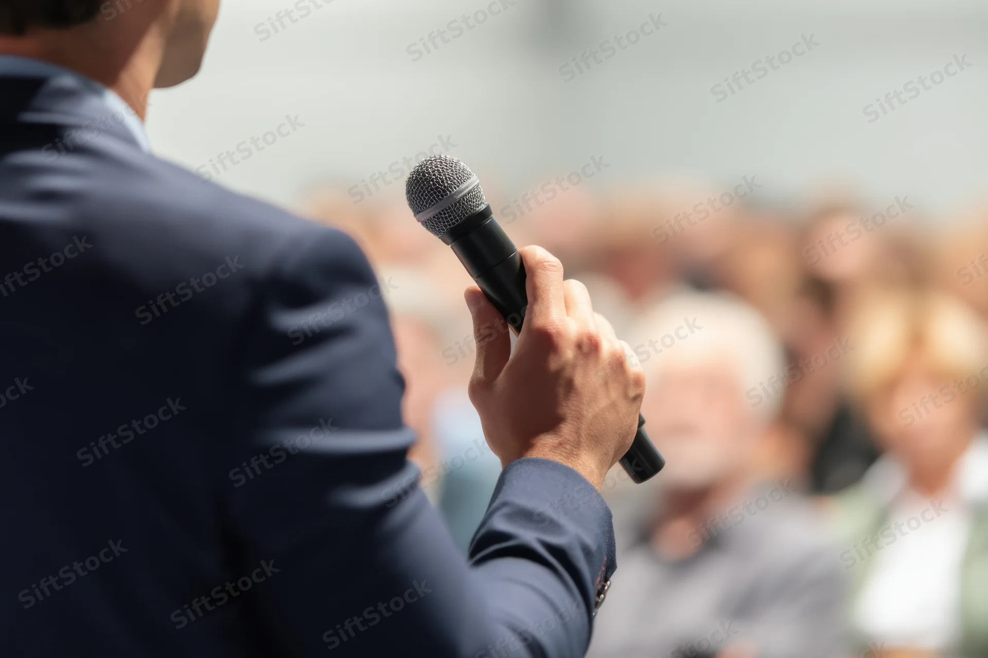 Man in business suit holding microphone while speaking to audience at corporate event