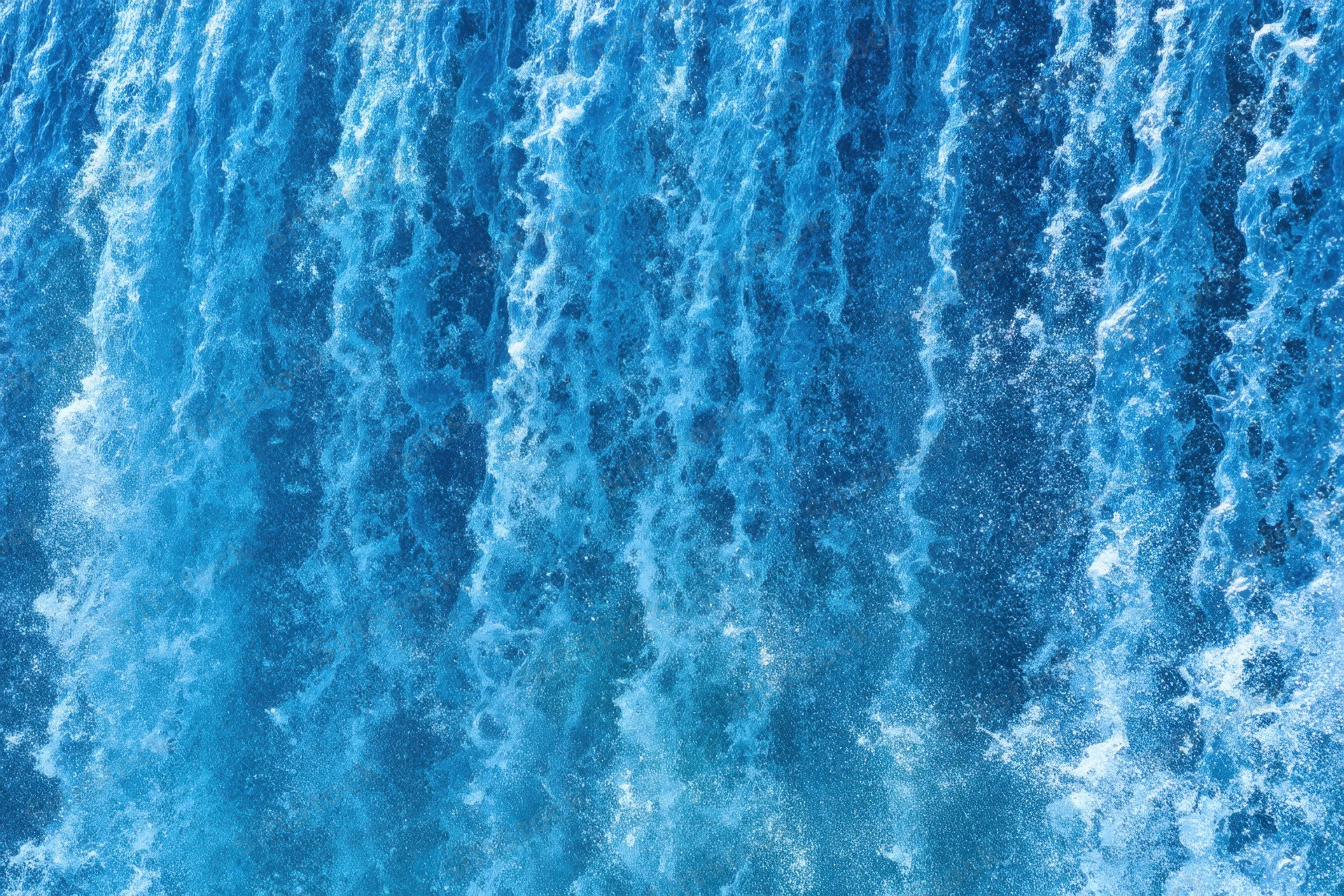Cascading waterfall flowing down in vibrant blue and white foam, viewed from above