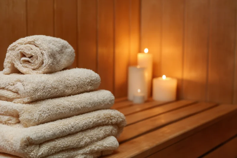 Folded white towels stacked on wooden bench in sauna with lit candles nearby