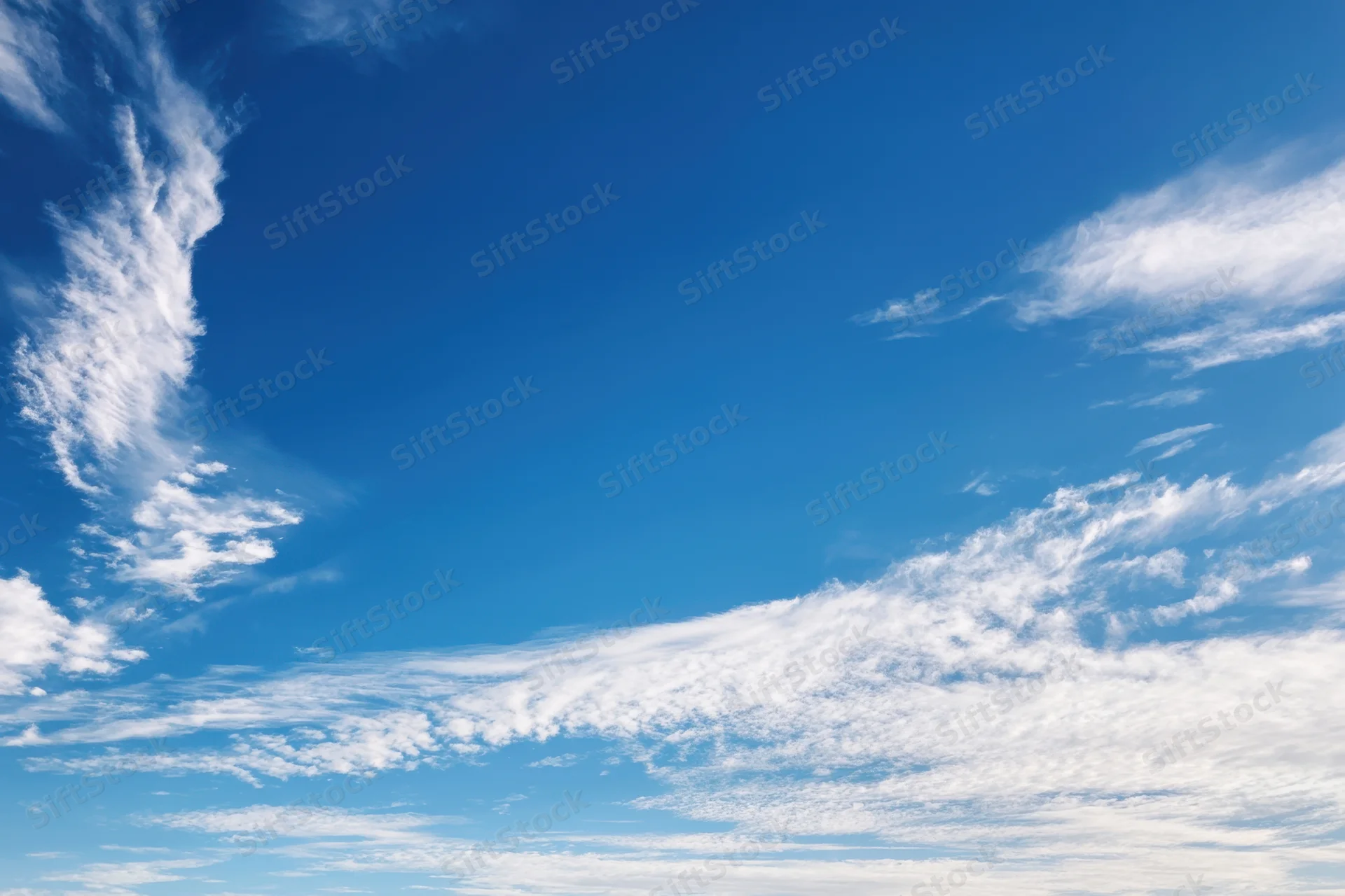 Vast clear blue sky with delicate wispy white clouds scattered across the horizon