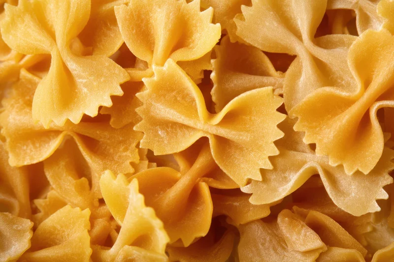 Uncooked farfalle pasta arranged in a dense closeup view showing detailed texture and shape