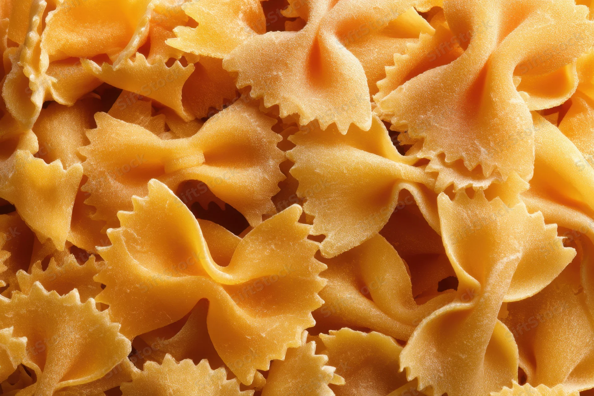 Uncooked farfalle pasta piled closely together in a textured arrangement