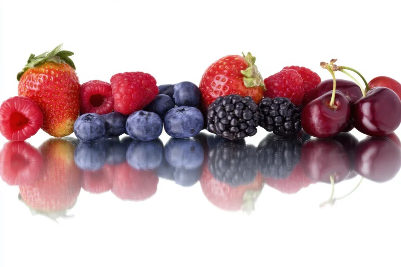 A row of fresh berries arranged on a reflective white surface showing their vibrant colors and glossy textures with mirror reflections below