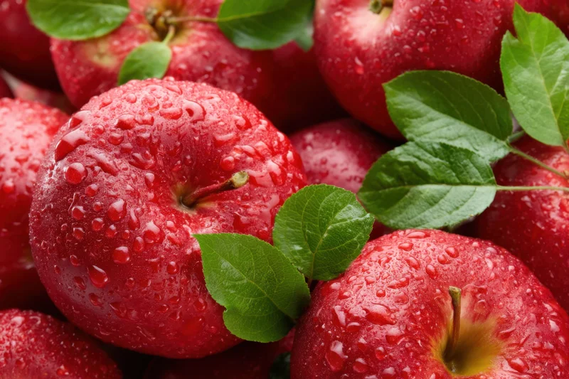 Freshly picked red apples glistening with water droplets and green leaves, piled together in a close-up view