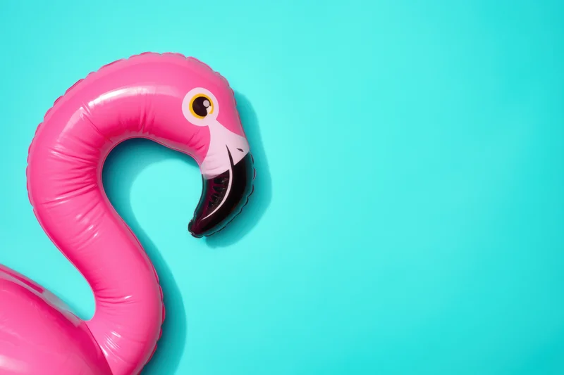Inflatable pink flamingo float resting on a bright turquoise background with copyspace