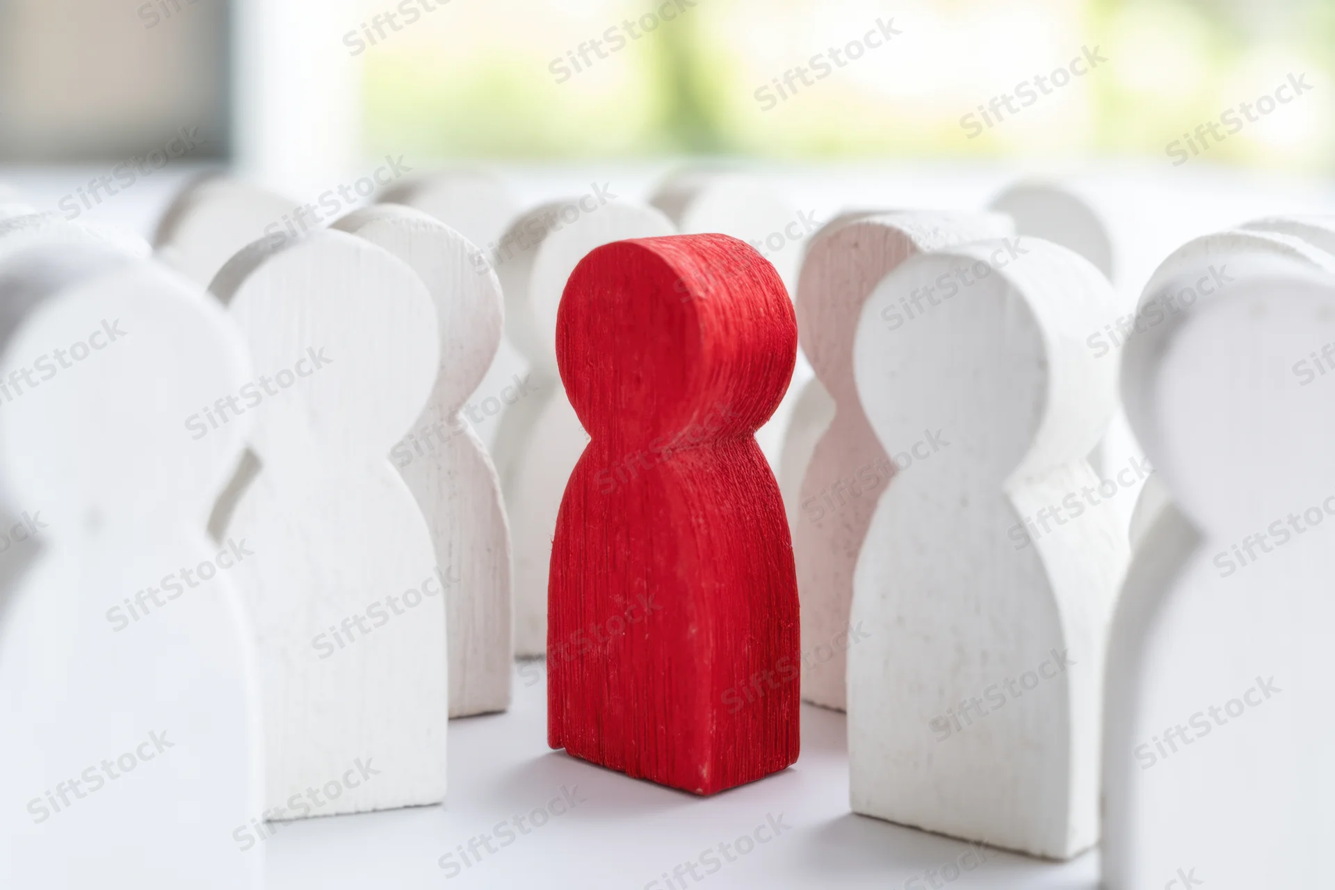 Red wooden figure standing among white figures on a light surface