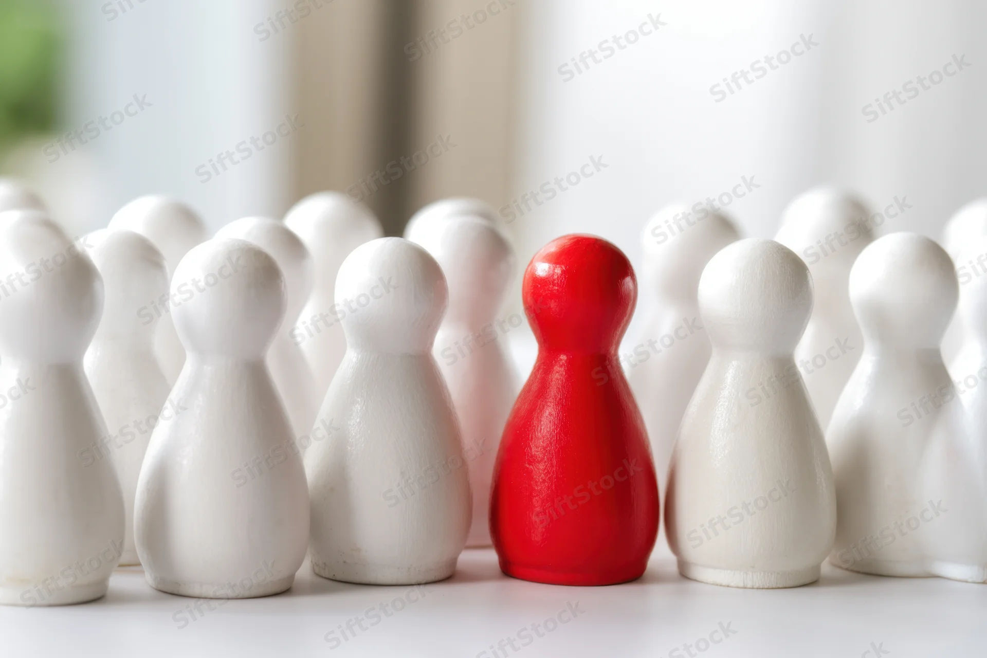 Red wooden figure standing among white figures on a light surface