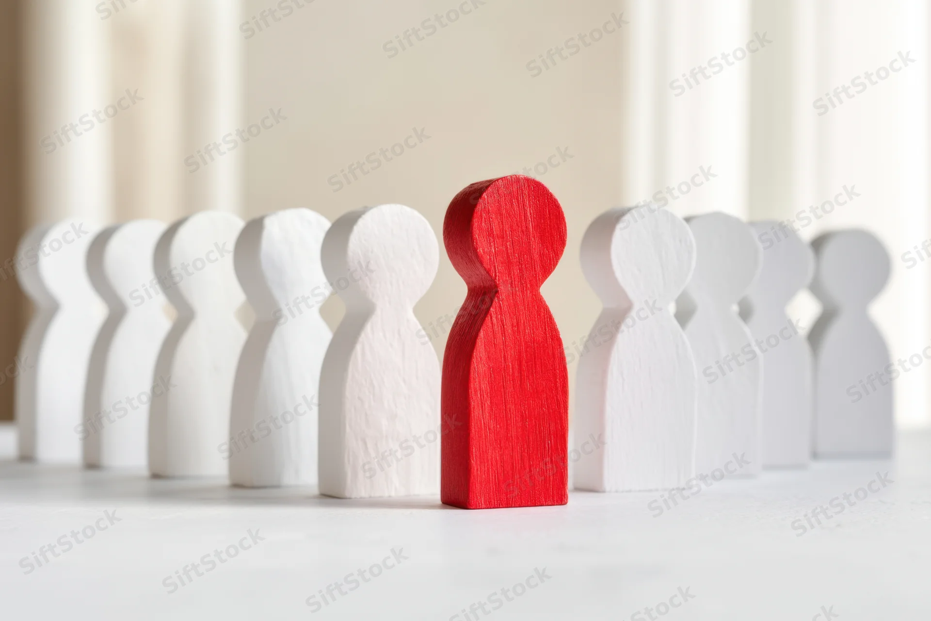Red wooden figure standing among white figures in a row on a light surface