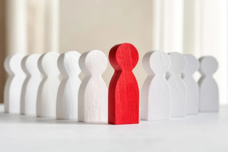 Red wooden figure standing among white figures in a row on a light surface