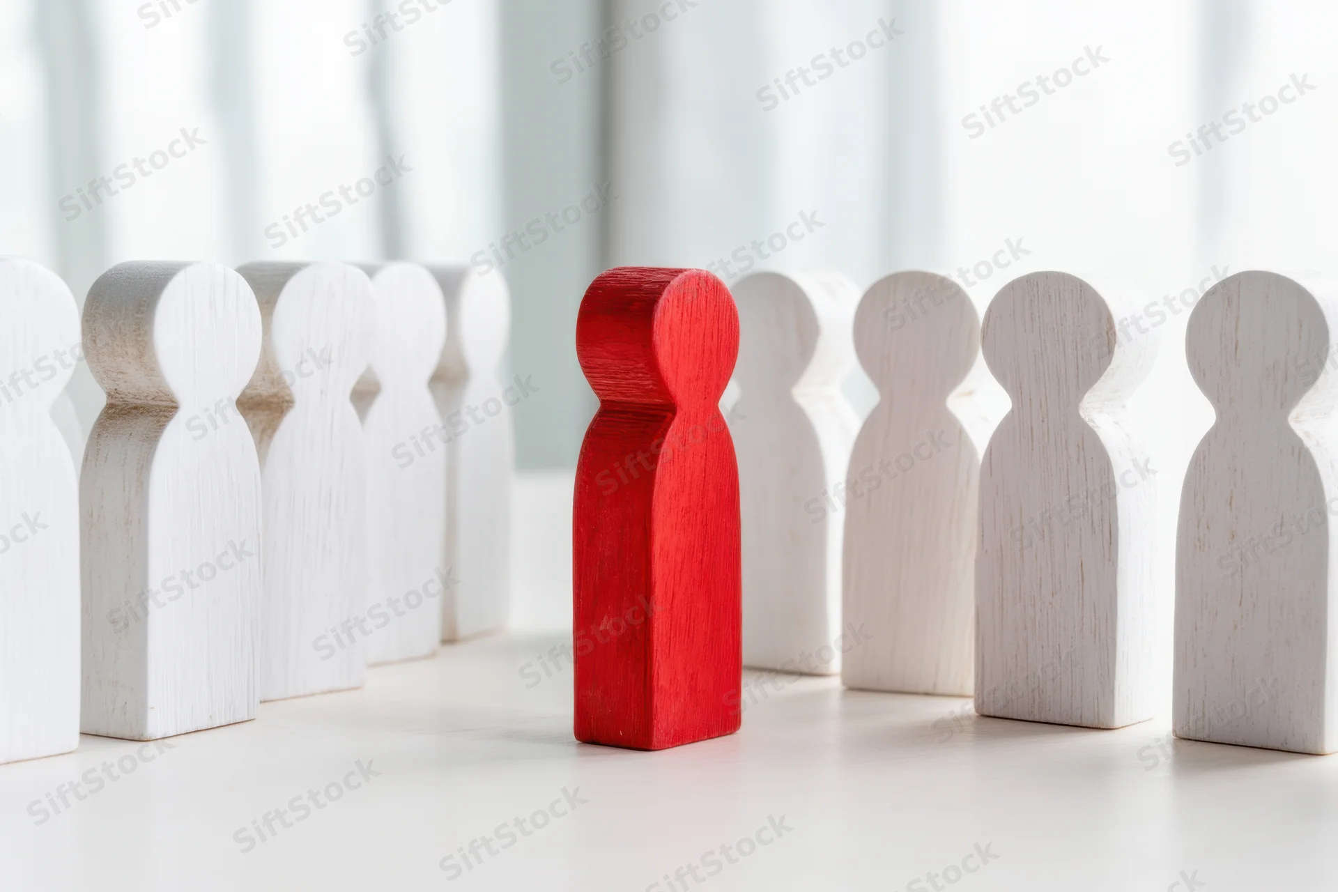 Red wooden figure standing among white figures in a row on a light surface