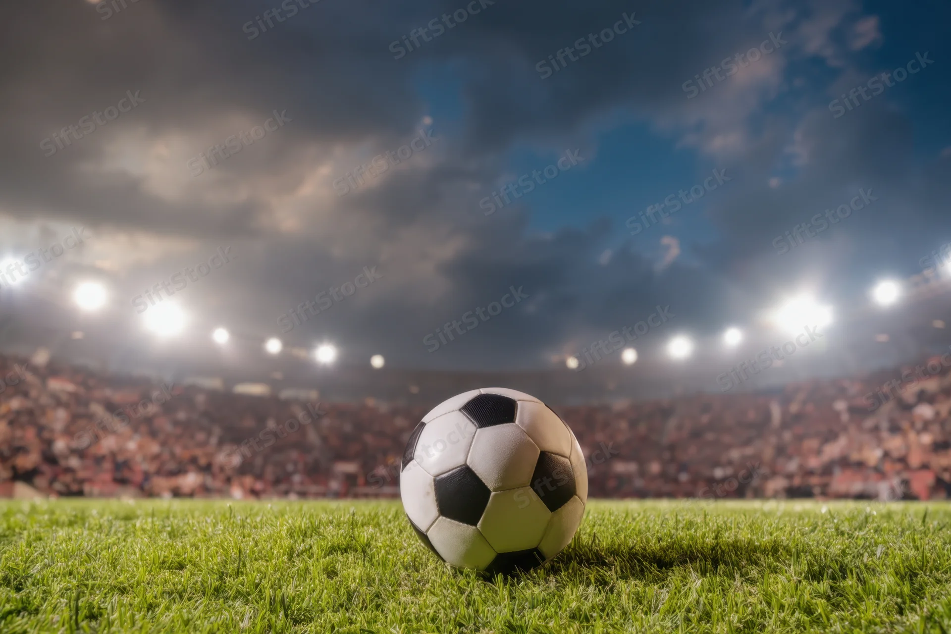 Soccer ball resting on grass field in front of stadium crowd under floodlights at night