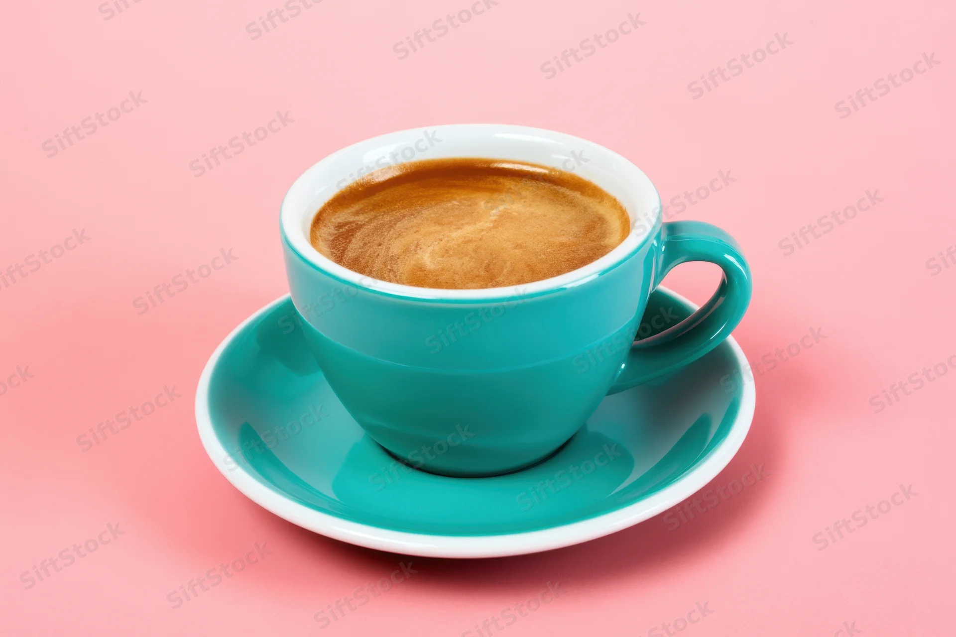 Turquoise ceramic coffee cup with saucer on pink background