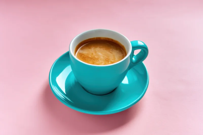 Turquoise coffee cup with saucer on pink background