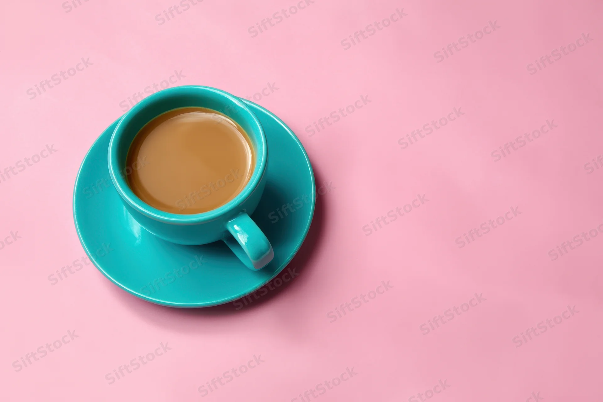Turquoise coffee cup and saucer on pink background in flat lay overhead view