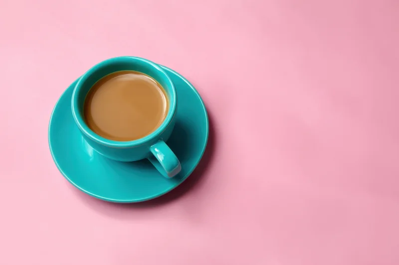 Turquoise coffee cup and saucer on pink background in flat lay overhead view