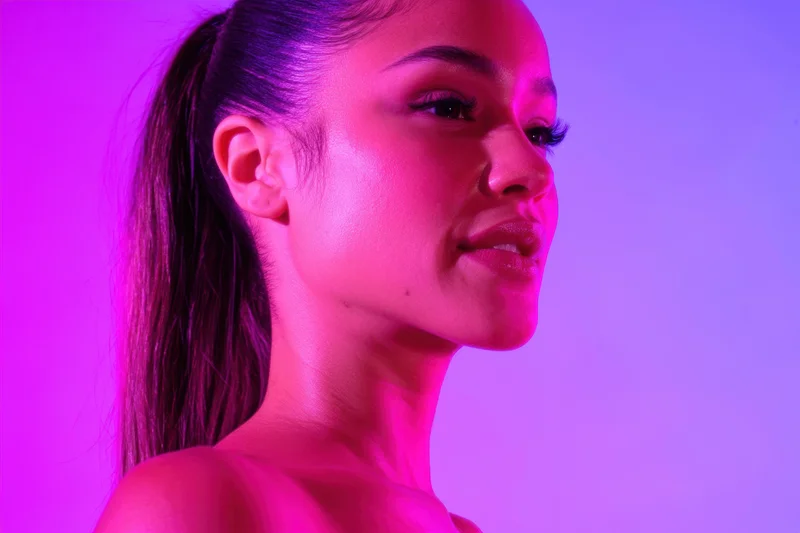 Woman in profile with sleek ponytail under pink and purple neon lighting
