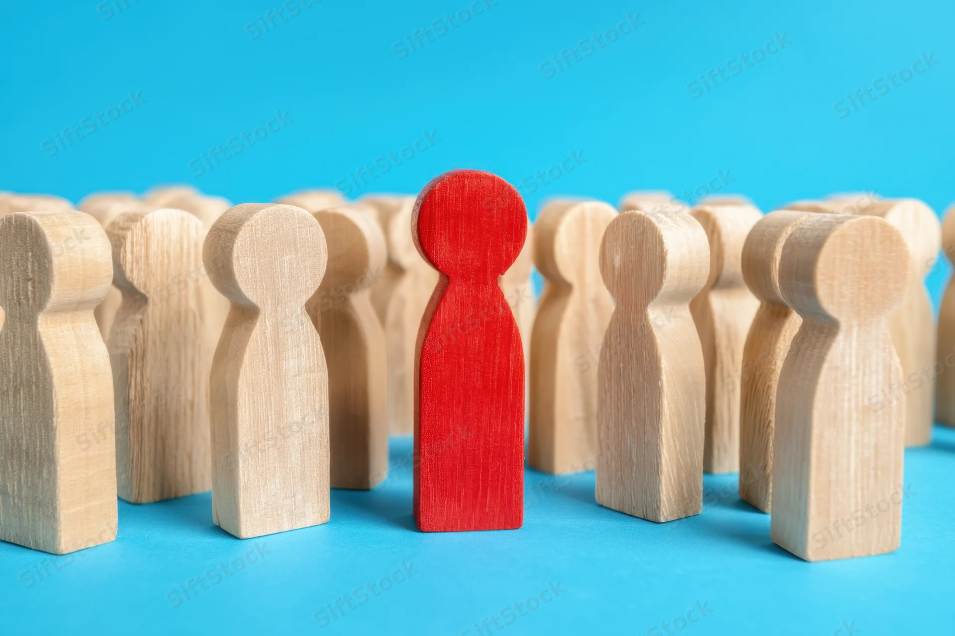 Red wooden figure standing among a group of beige figures on a blue background