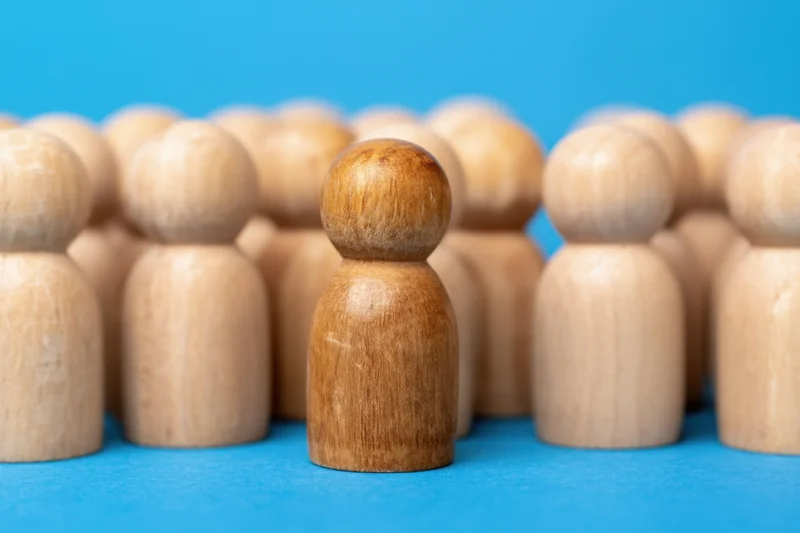 Wooden figure standing out in front of a group of similar figures on a blue surface