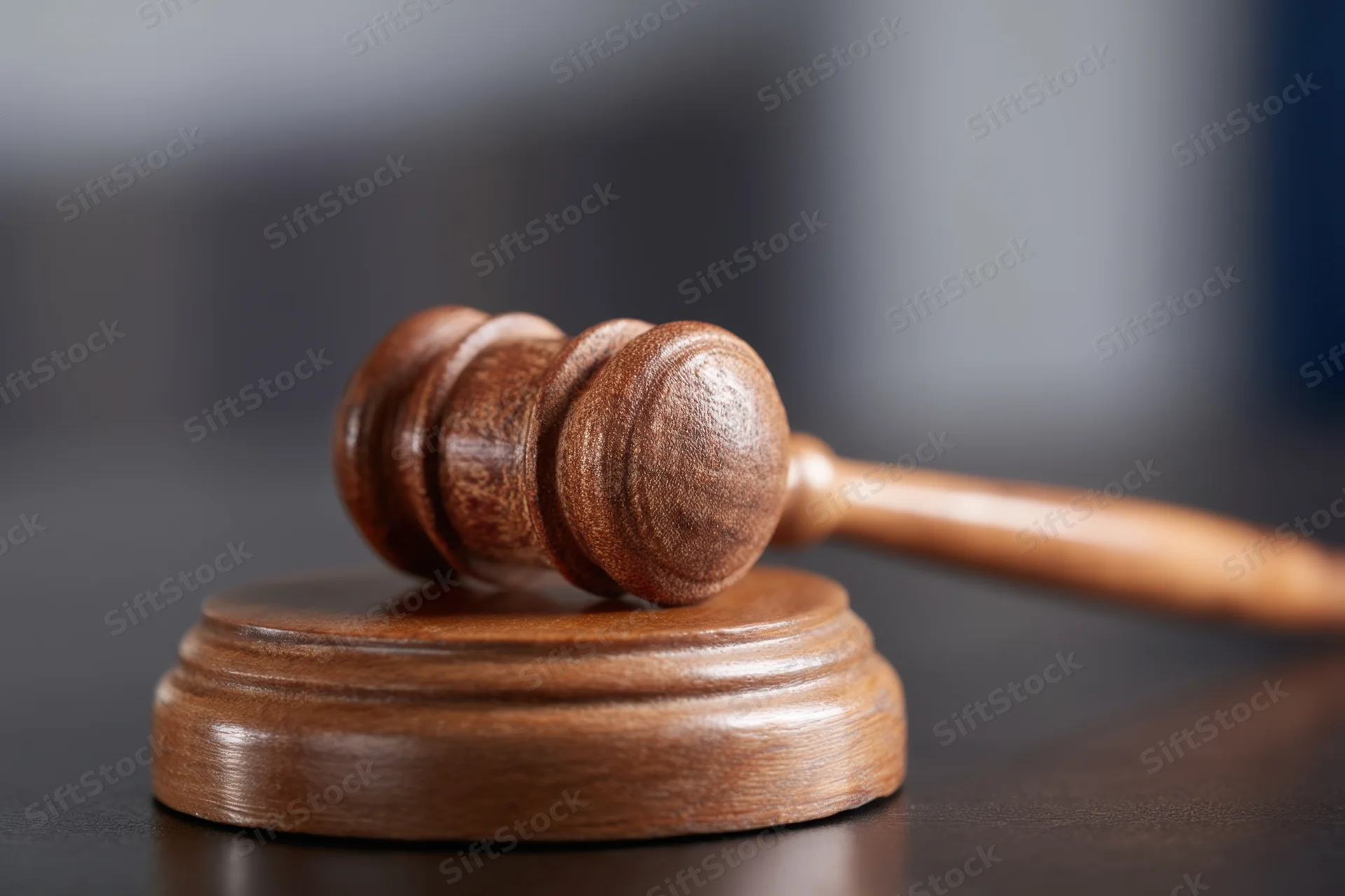 Wooden gavel resting on dark surface with shallow depth of field, closeup view of handle and soundblock