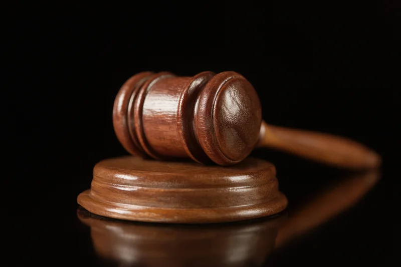 Wooden gavel resting on round base against black background with reflection
