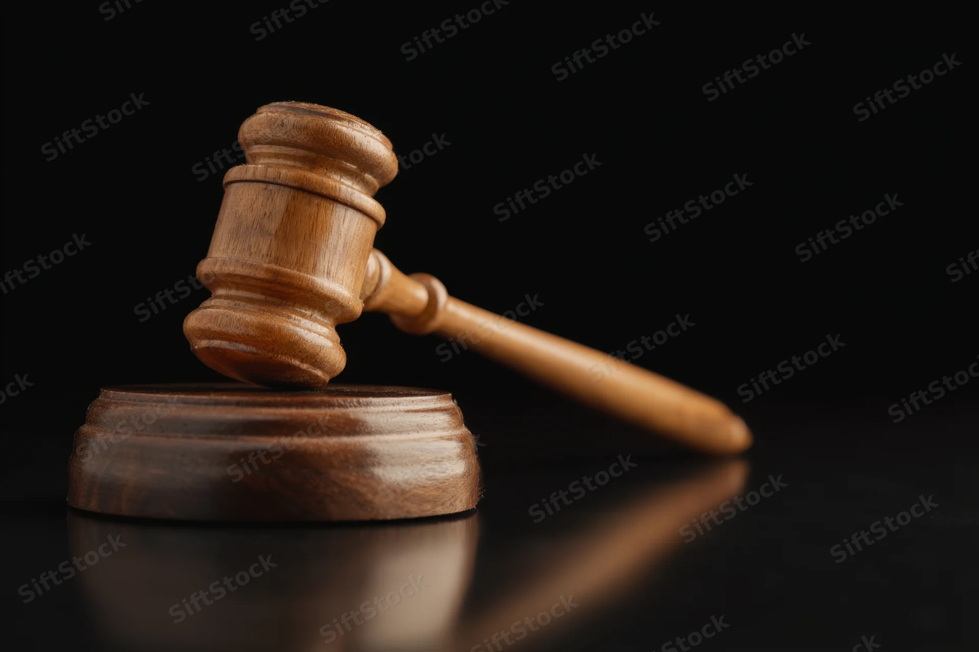 Wooden gavel resting on round base against black reflective surface