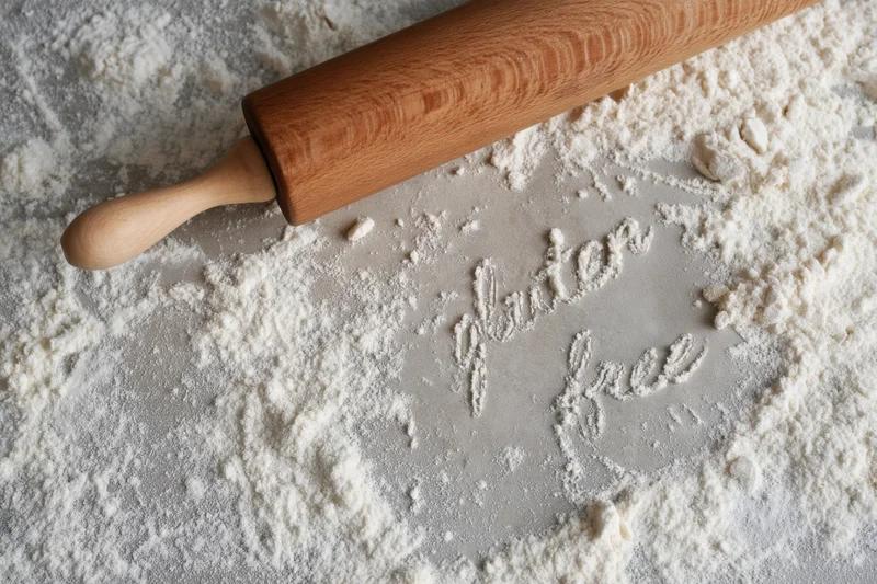 Wooden rolling pin resting on a flour-dusted countertop with "gluten free" written in the flour