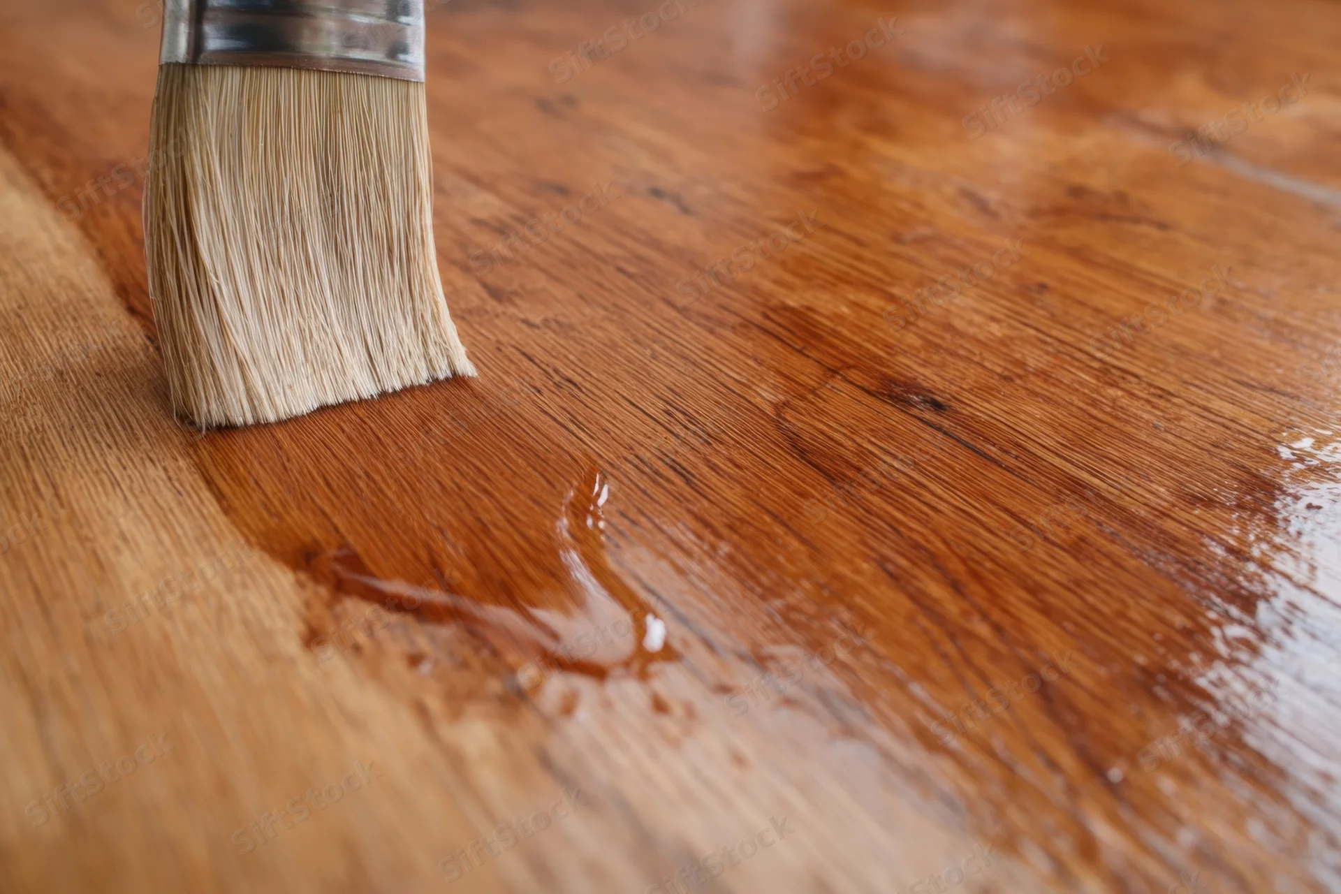 A brush applying wood finish to a wooden surface showing the grain and sheen