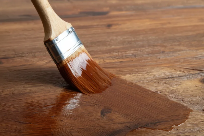 Brush applying wood stain to a wooden surface showing grain and sheen