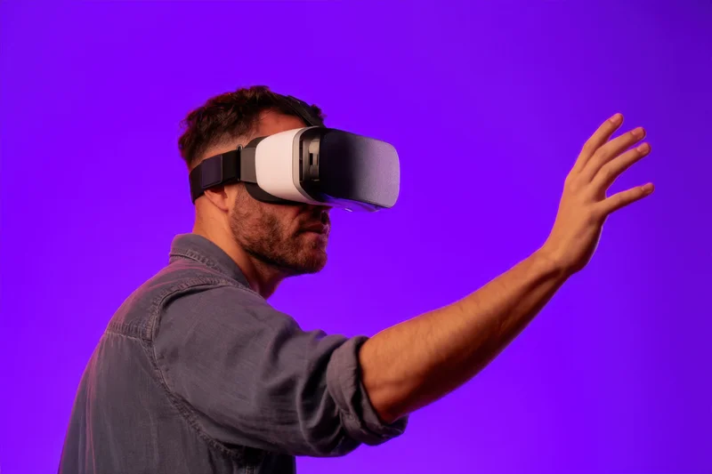 Young man wearing virtual reality headset reaching out with hand against purple background