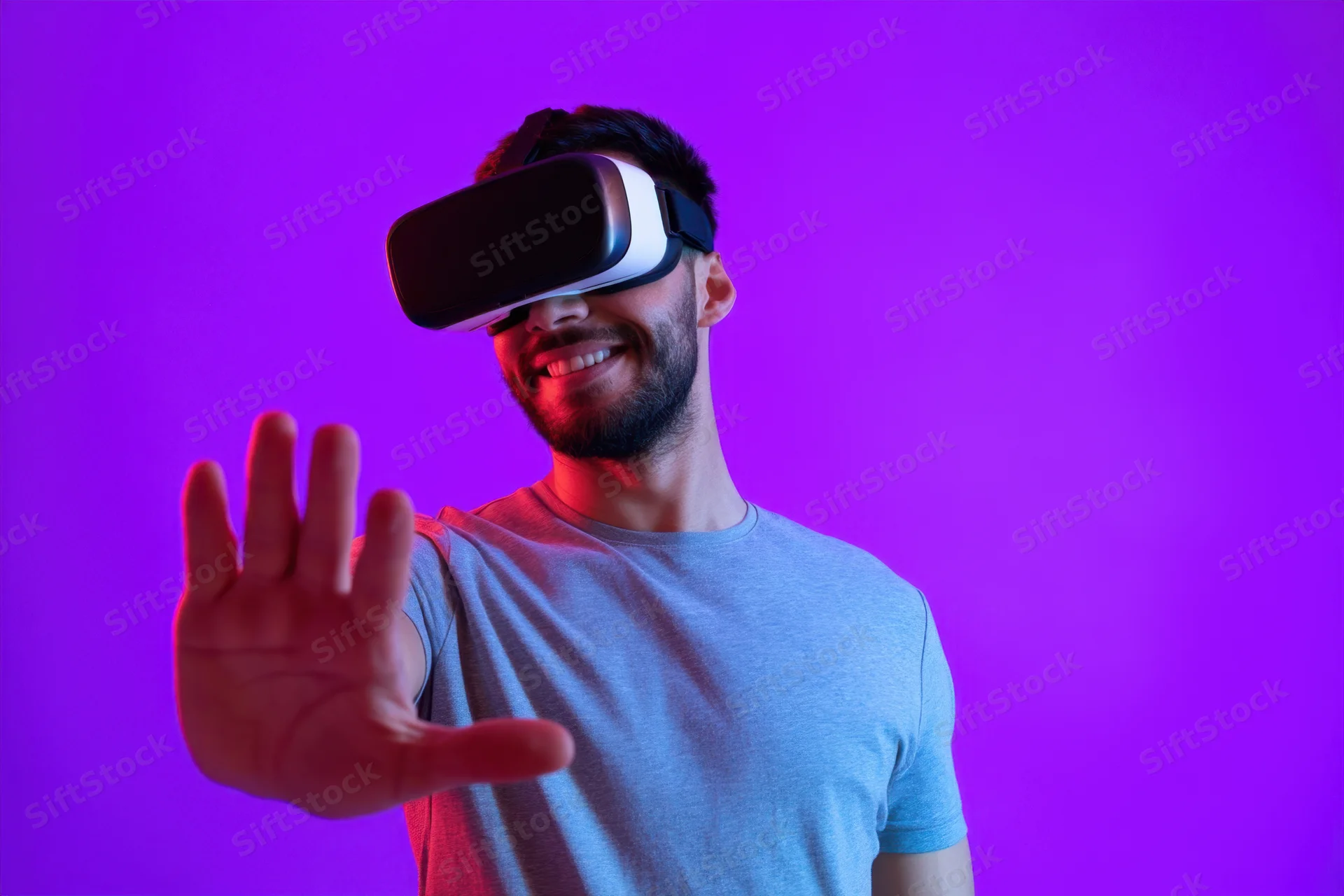 Young man wearing virtual reality headset smiling and gesturing with hand against purple background