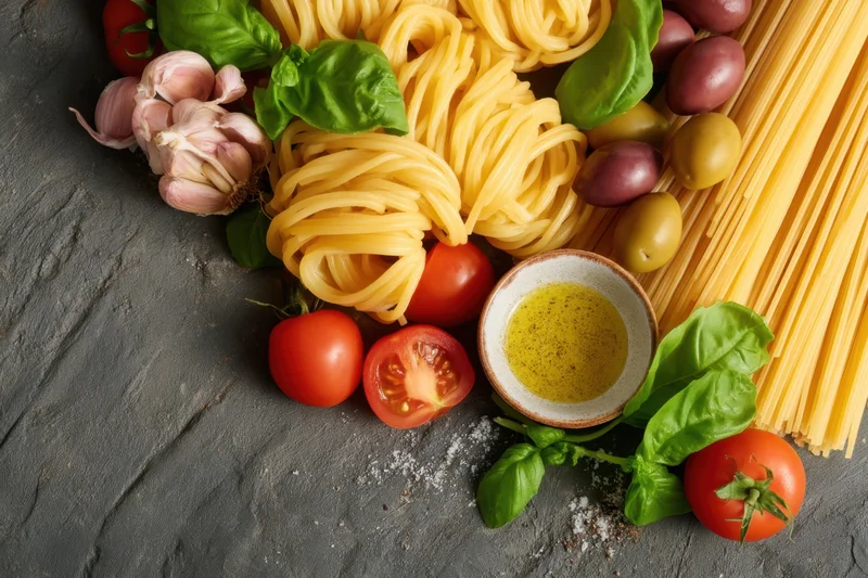 Uncooked pasta and fresh ingredients arranged on a dark textured surface