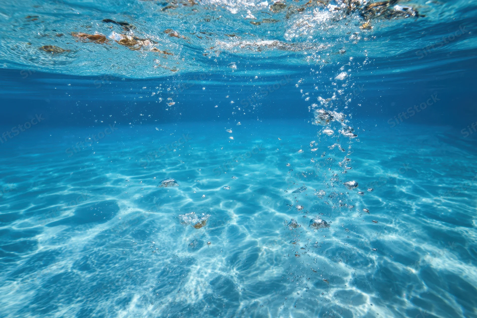 Clear blue water with rising bubbles and light patterns on the ocean floor