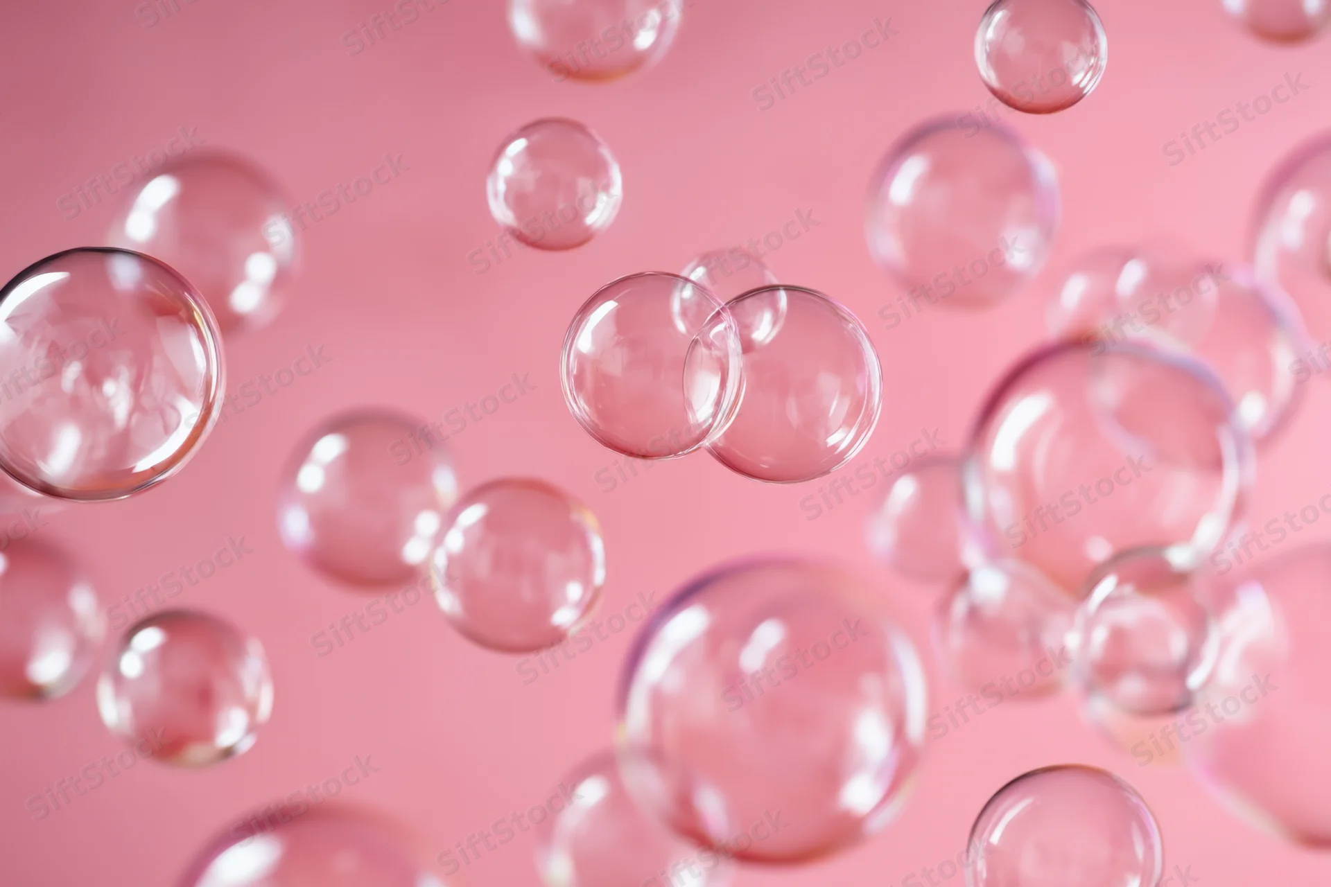 Translucent soap bubbles floating against a soft pink background with shallow depth of field
