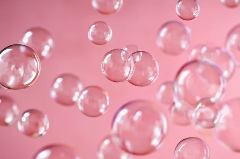 Translucent soap bubbles floating against a soft pink background with shallow depth of field