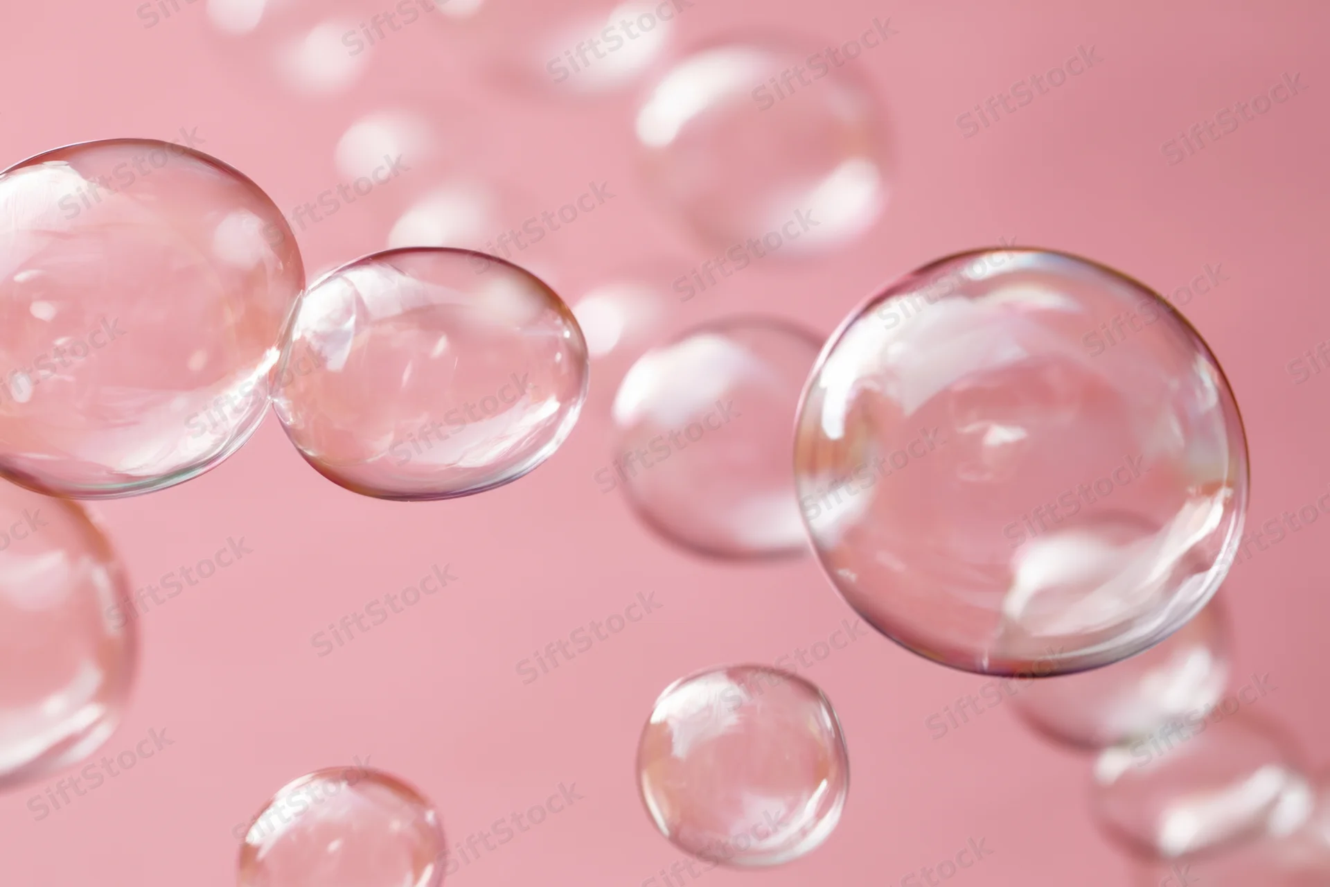 Translucent soap bubbles floating against a soft pink background