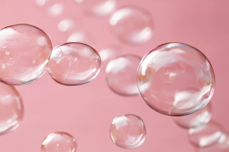 Translucent soap bubbles floating against a soft pink background